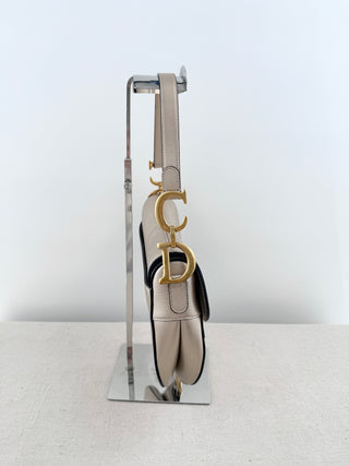 Christian Dior saddle bag crafted in grained calfskin leather featuring asymmetrical saddle silhouette, front flap closure, and oversized antique "D" charm