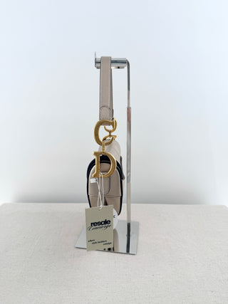 Christian Dior saddle bag crafted in grained calfskin leather featuring asymmetrical saddle silhouette, front flap closure, and oversized antique "D" charm