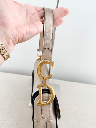 Christian Dior saddle bag crafted in grained calfskin leather featuring asymmetrical saddle silhouette, front flap closure, and oversized antique "D" charm