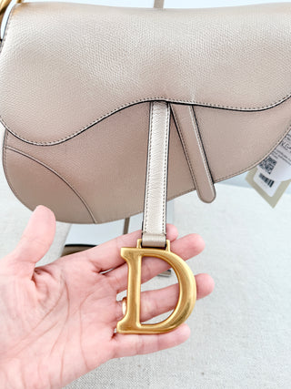 Christian Dior saddle bag crafted in grained calfskin leather featuring asymmetrical saddle silhouette, front flap closure, and oversized antique "D" charm
