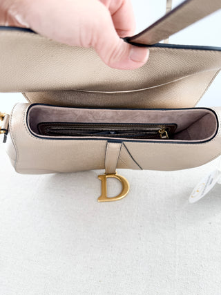 Christian Dior saddle bag crafted in grained calfskin leather featuring asymmetrical saddle silhouette, front flap closure, and oversized antique "D" charm