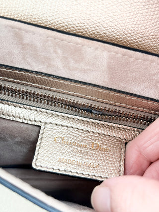 Christian Dior saddle bag crafted in grained calfskin leather featuring asymmetrical saddle silhouette, front flap closure, and oversized antique "D" charm